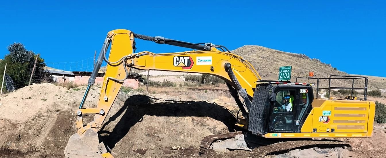 Excavadora sobre orugas cortando un montículo de tierra bajo cielo despejado