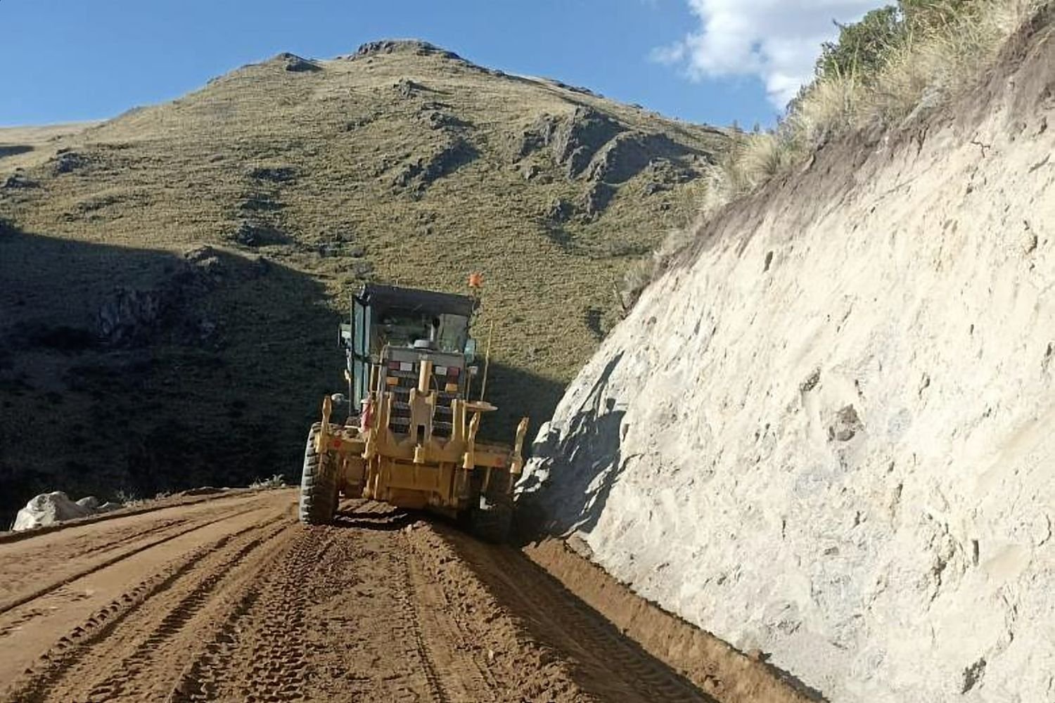 Motoniveladora perfilando una vía junto a un talud de corte