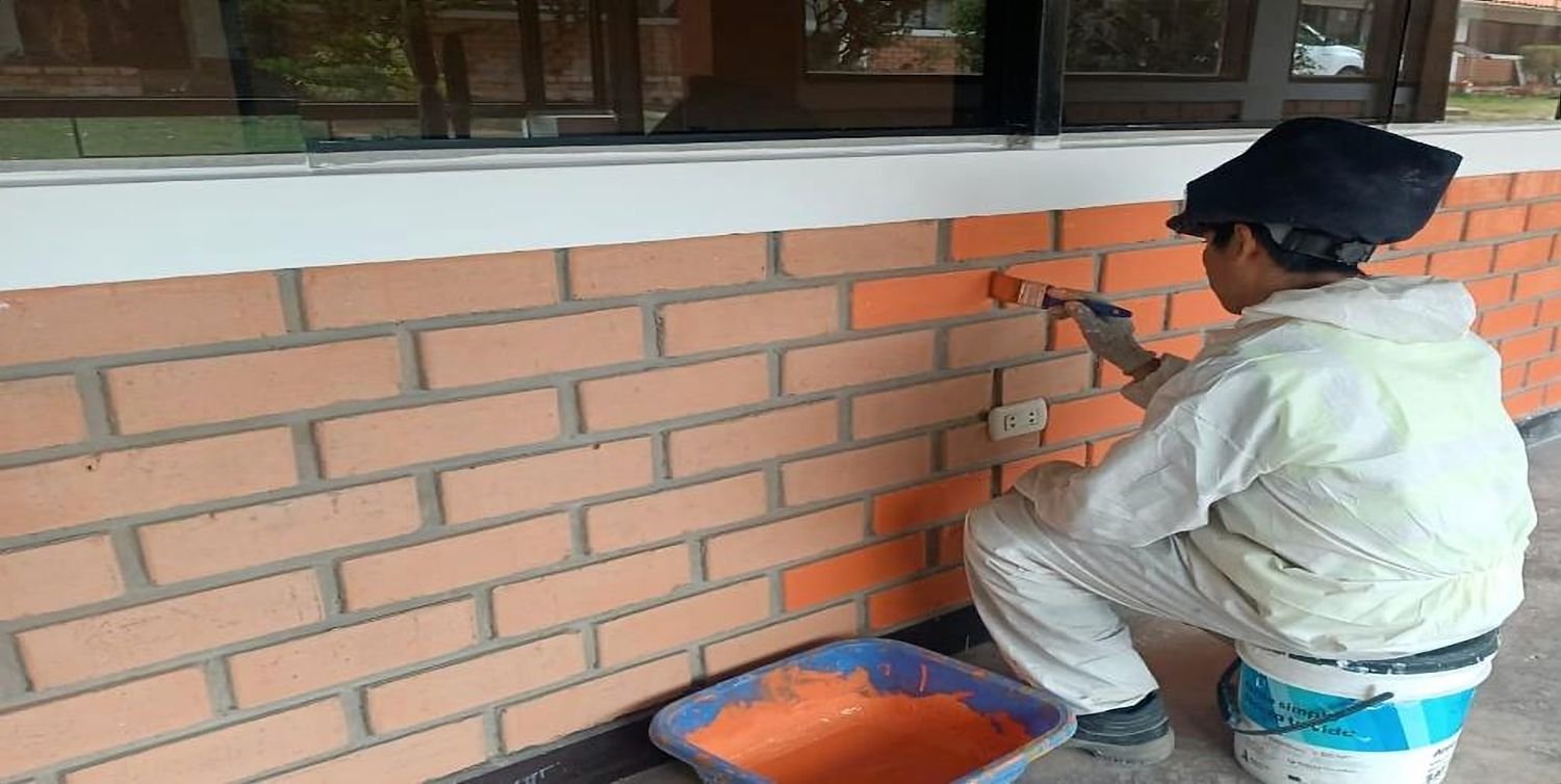 Trabajadora pintando un muro de ladrillo caravista