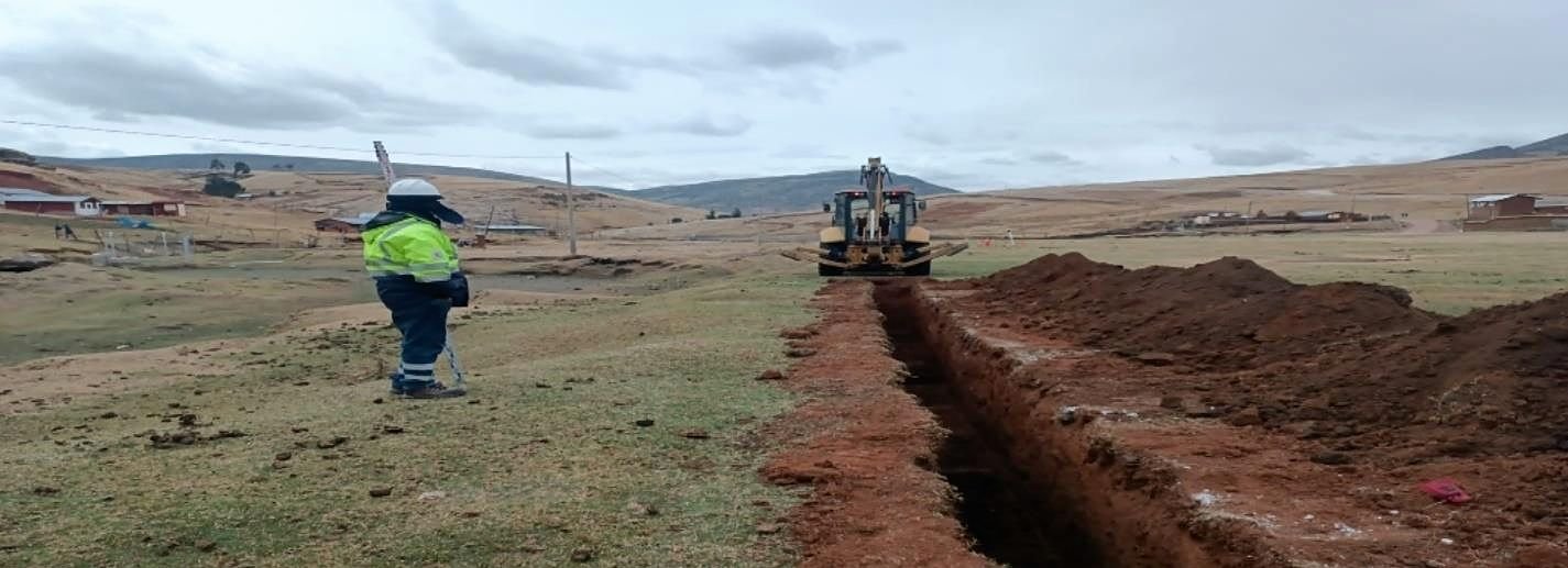 Zanja recién excavada con retroexcavadora al fondo